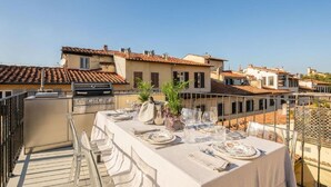 A rooftop terrace with a dining table set for four, a grill, and a view of surrounding buildings. - Exclusive Florence Getaway with Jacuzzi, Terraces & Concierge Services (Firenze)