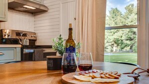 Cozinha com bancada de madeira, uma garrafa de vinho, um copo de vinho e uma tábua de queijos.