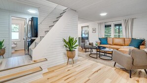 Um interior moderno com escada, área de estar com sofá e mesa de centro, e cozinha com geladeira e pia.