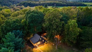 Uma cabana isolada rodeada por uma floresta densa, com um alpendre bem iluminado e uma vista desobstruída da paisagem circundante.