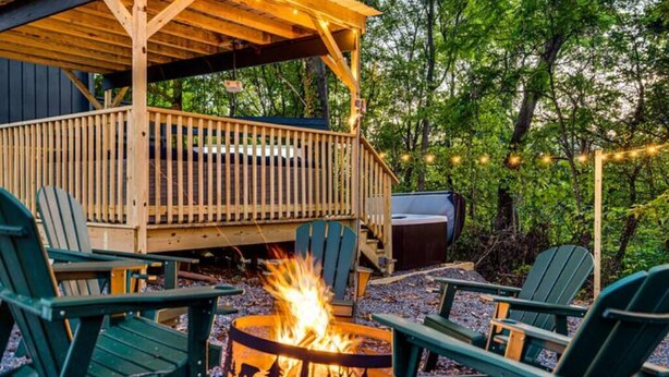 Um deck de madeira com cadeiras Adirondack, uma lareira e luzes de corda.