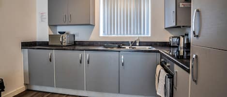 A modern kitchen with grey cabinets, a built-in oven, a microwave, and a window with blinds.