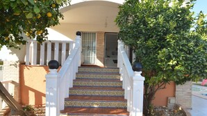 A staircase with patterned tiles leading to a door, flanked by white railings and a tree with green leaves. - Villa Amore Mio South (Orihuela Costa)
