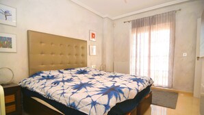 A bedroom with a large bed, a headboard, a bedside table, a mirror, and a window with curtains. - Villa Amore Mio South (Orihuela Costa)