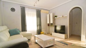 A living room with a sofa, a coffee table, a TV on a stand, and a small table with chairs. - Villa Amore Mio South (Orihuela Costa)