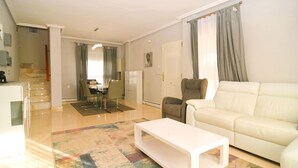 Een moderne woonkamer met een witte bank, een salontafel en een eethoek met een tafel en stoelen.