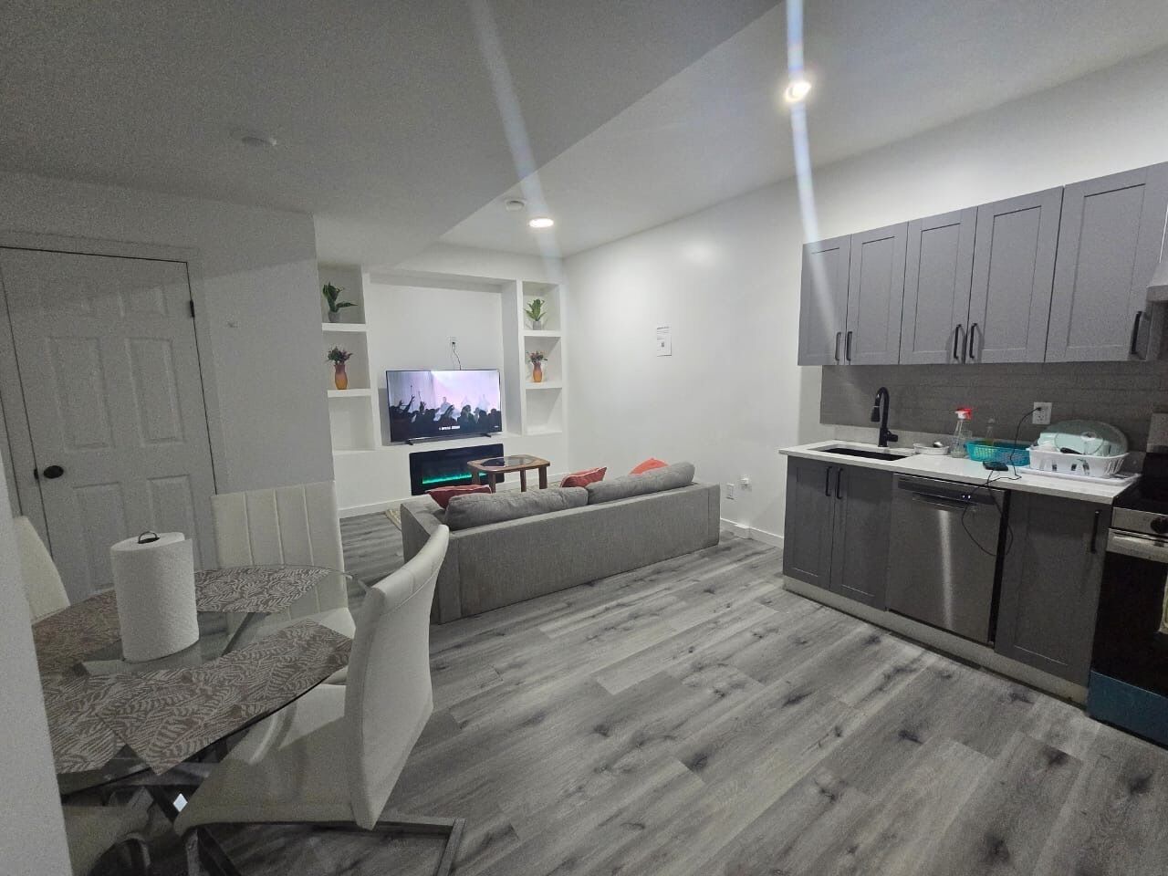 A modern kitchen with grey cabinets, a dining area with a table and chairs, and a grey sofa.