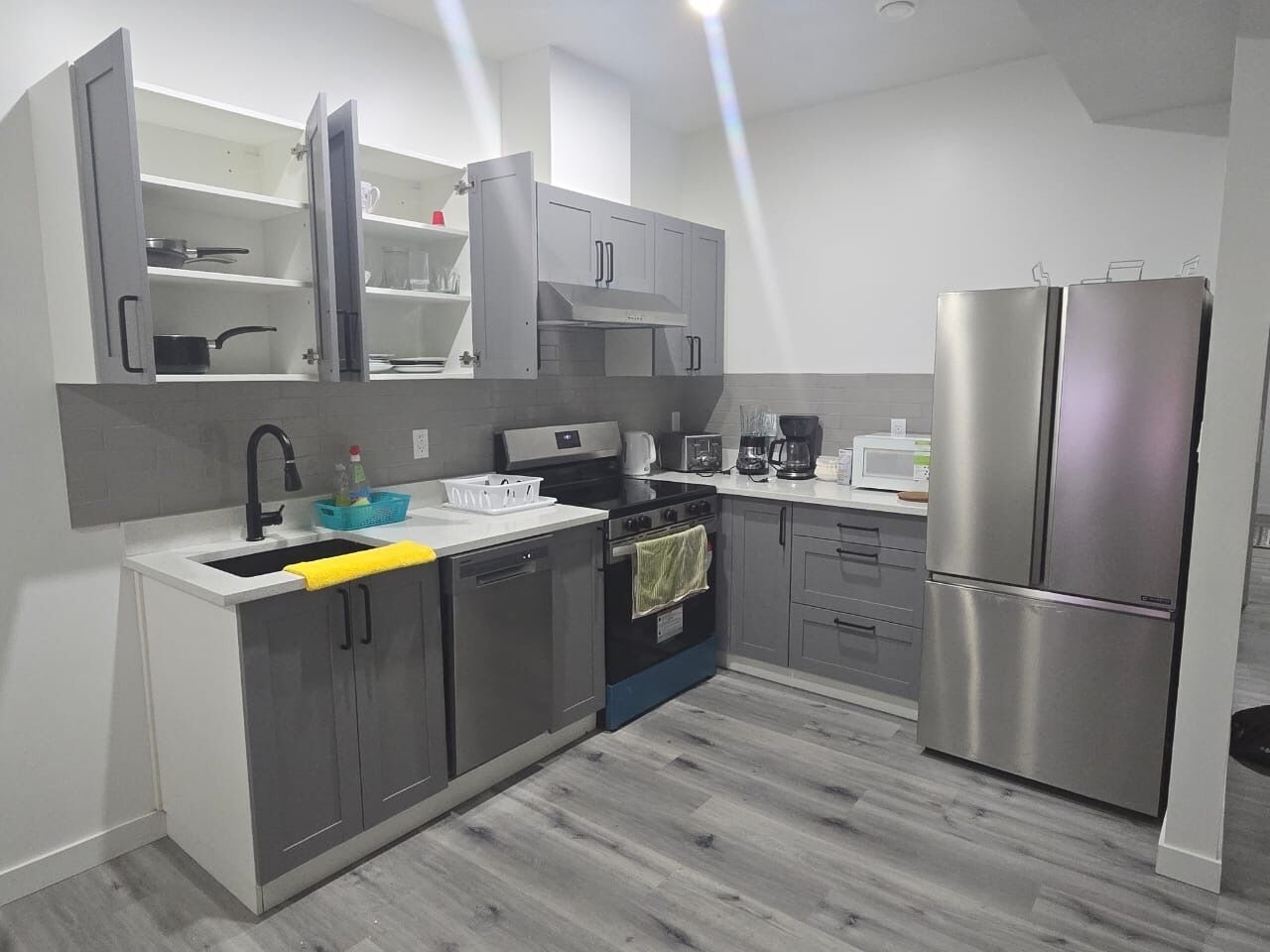 A modern kitchen with grey cabinets, a stainless steel refrigerator, a built-in oven, and a microwave.