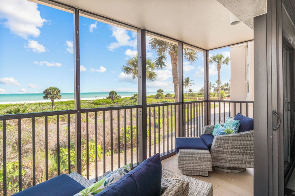 Un balcon avec vue sur la plage et l’océan, aménagé avec des canapés et des coussins en osier.