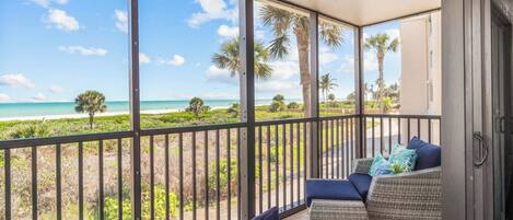 Un balcon avec vue sur la plage et l’océan, aménagé avec des canapés et des coussins en osier.