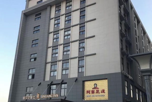 Ein mehrgeschossiges Gebäude mit einem Schild für 'JINJIANG INN' und einer großen Werbeanzeige an der Fassade.