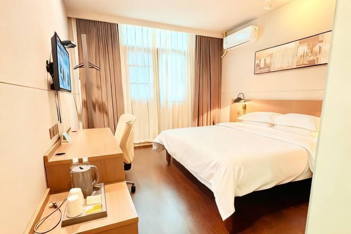 Ett hotellrum med en säng, ett skrivbord med en kaffebryggare, en stol och en tv på väggen.