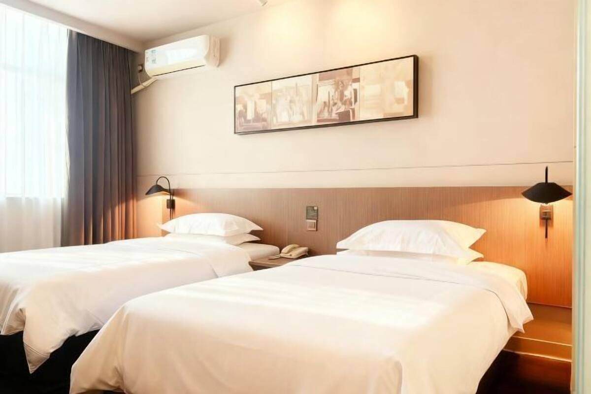 Ett hotellrum med två sängar, en väggmonterad luftkonditioneringsanläggning, en inramad tavla och en telefon vid sängen.