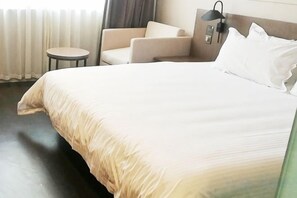Ein Hotelzimmer mit einem großen Bett, einem Sessel, einem kleinen Tisch und einer Lampe.