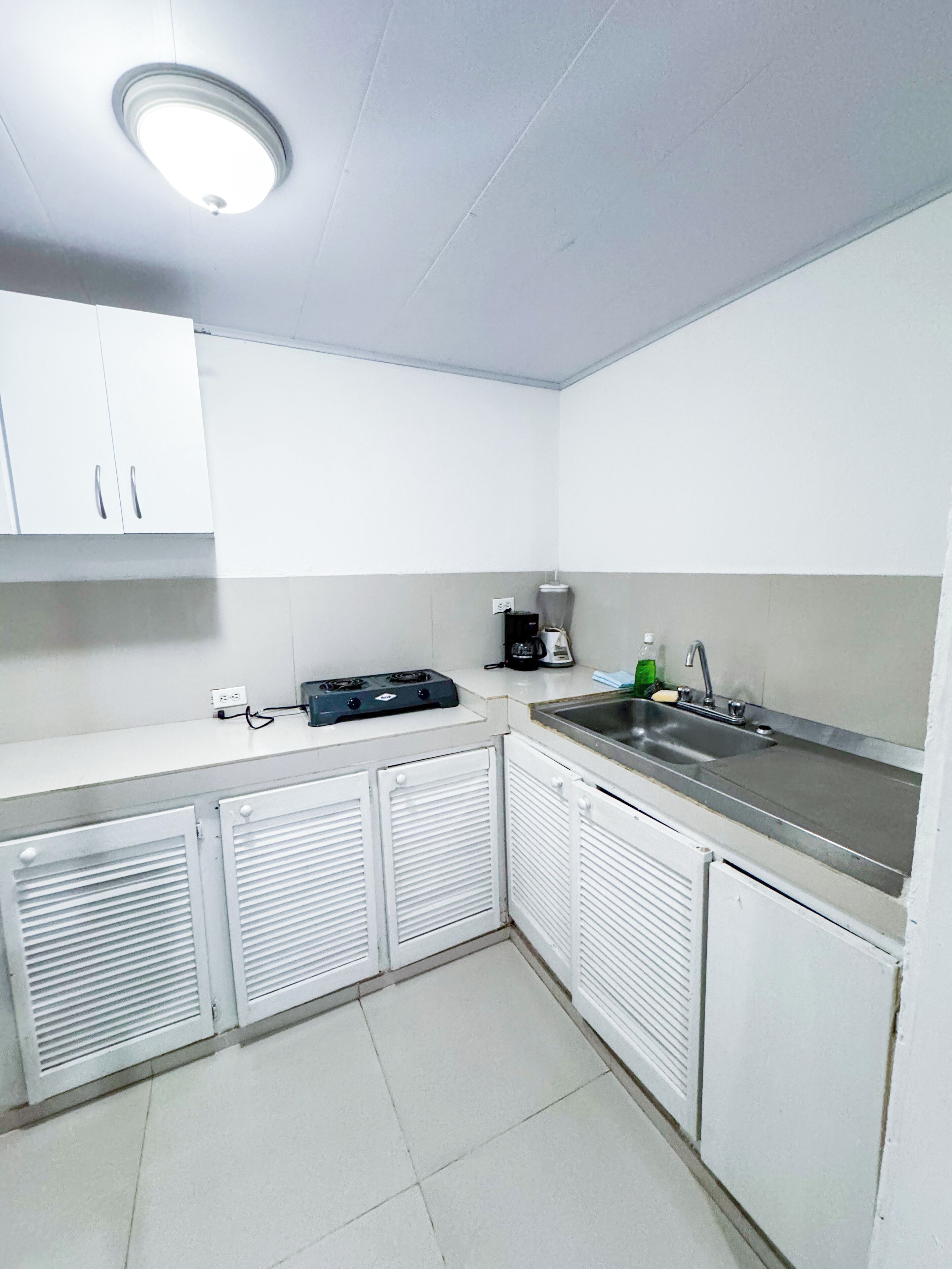 A small kitchen with white cabinets, a sink, a stove, and a ceiling light.