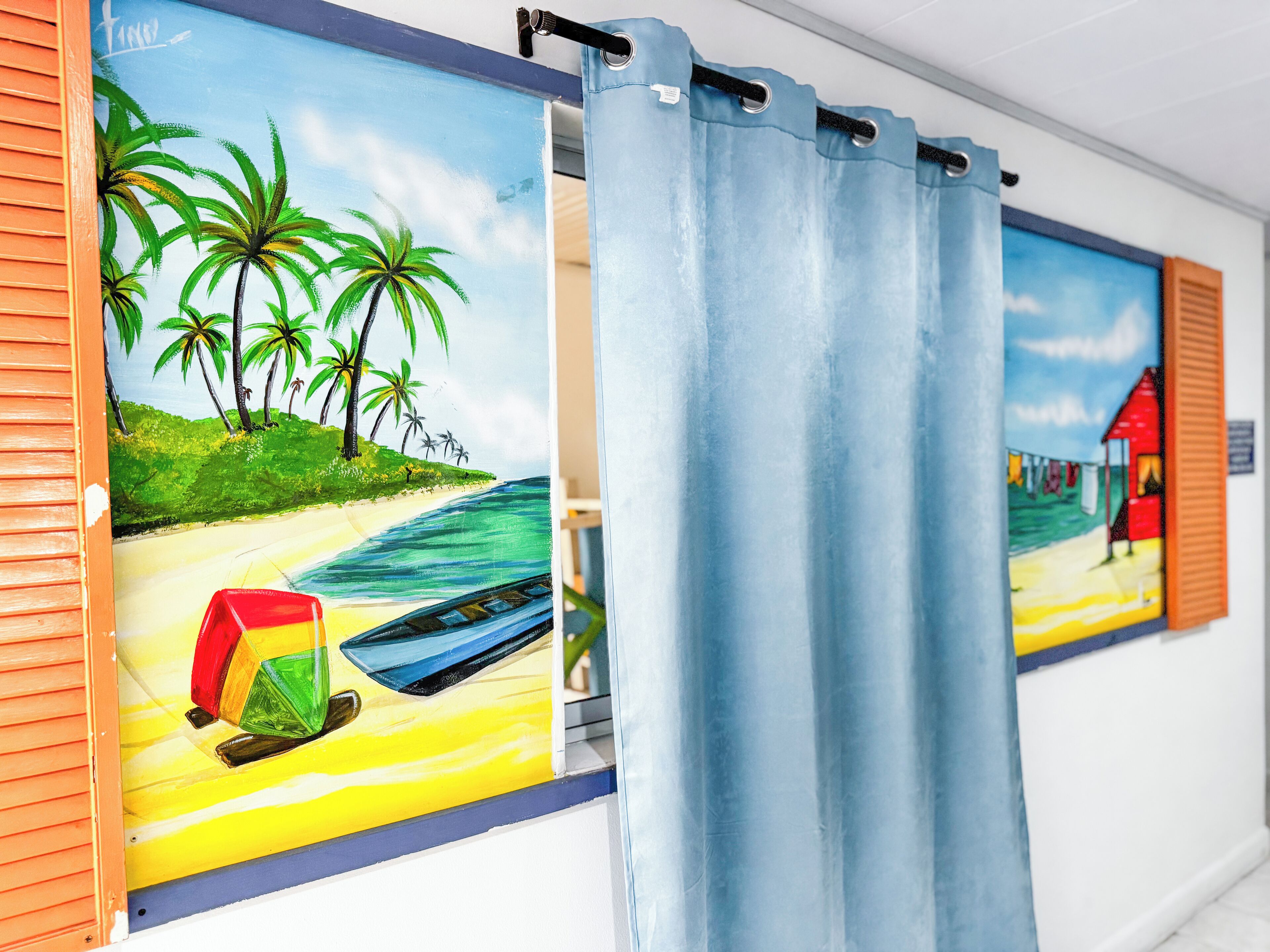 Una habitación con un cuadro de una escena de playa en la pared, una cortina y un pequeño barco modelo.
