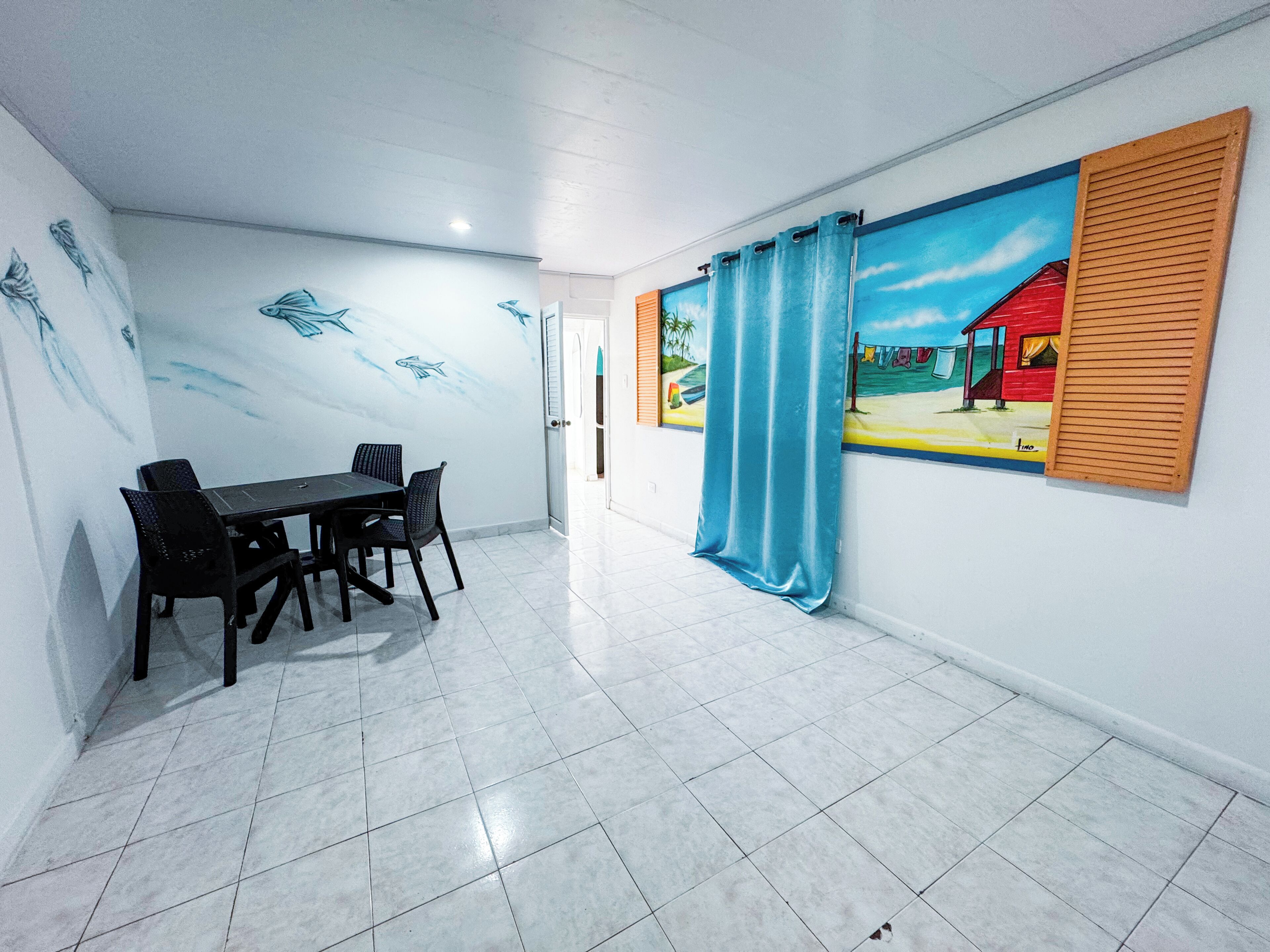 Un comedor con una mesa, sillas, un mural en la pared y una ventana con cortina.