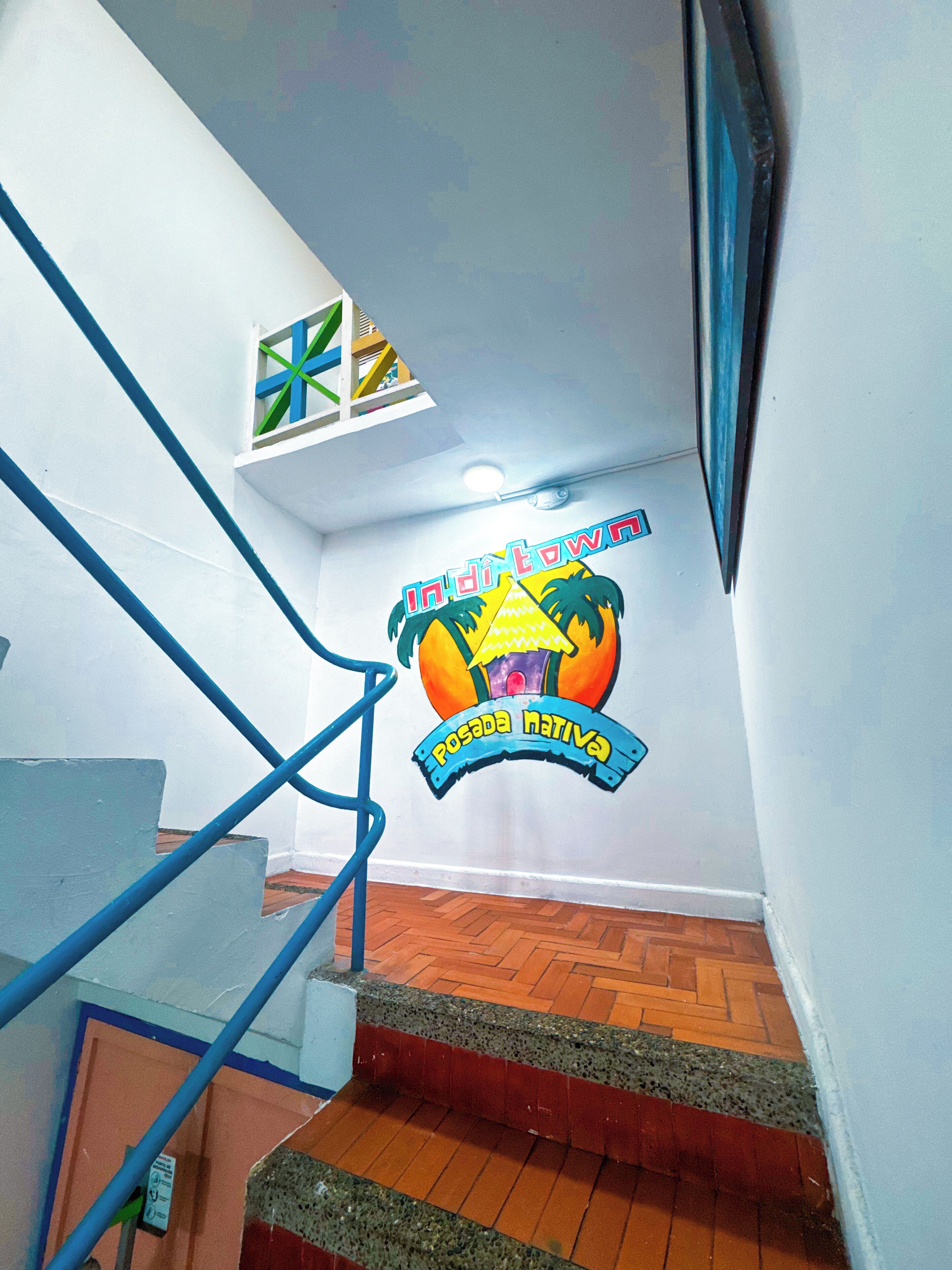 A staircase with blue handrails, a wooden floor, and a wall with a colorful logo.