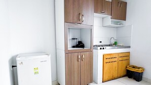 Una cocina compacta con un refrigerador blanco, armarios de madera, un lavamanos y un basurero.