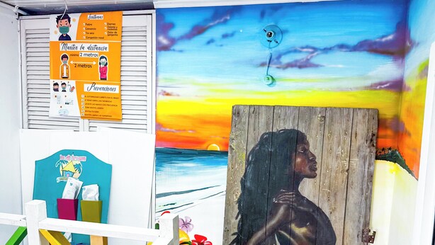 Una habitación con un mural de atardecer colorido, una puerta de madera con silueta y un cartel con pautas de salud.