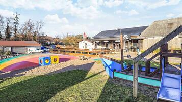 A playground with slides and play structures, a picnic area, and a building with a pirate-themed sign in the background.
