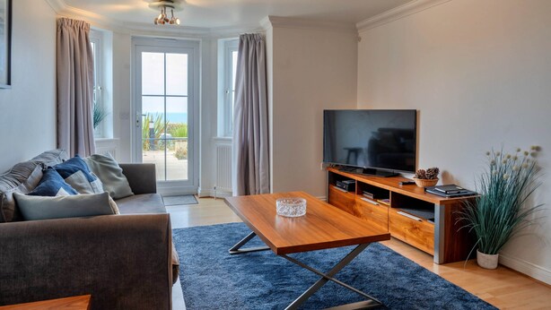 Uma sala de estar moderna com sofá, mesa de centro, televisão e vista para o exterior.