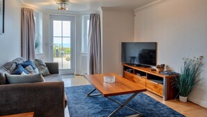 Un salon moderne avec un canapé, une table basse, un téléviseur et une vue sur l’extérieur.