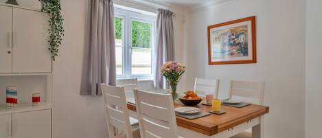 A dining area with a wooden table, white chairs, a vase with flowers, and a painting on the wall.
