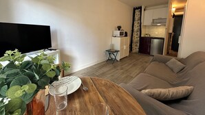 Een woonkamer met een flatscreen televisie, een houten salontafel, een beige bank en een kleine eettafel met een bord en glas.