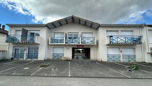 Een gebouw met twee verdiepingen, een plat dak, meerdere balkons met blauwe leuningen en een parkeerplaats ervoor.