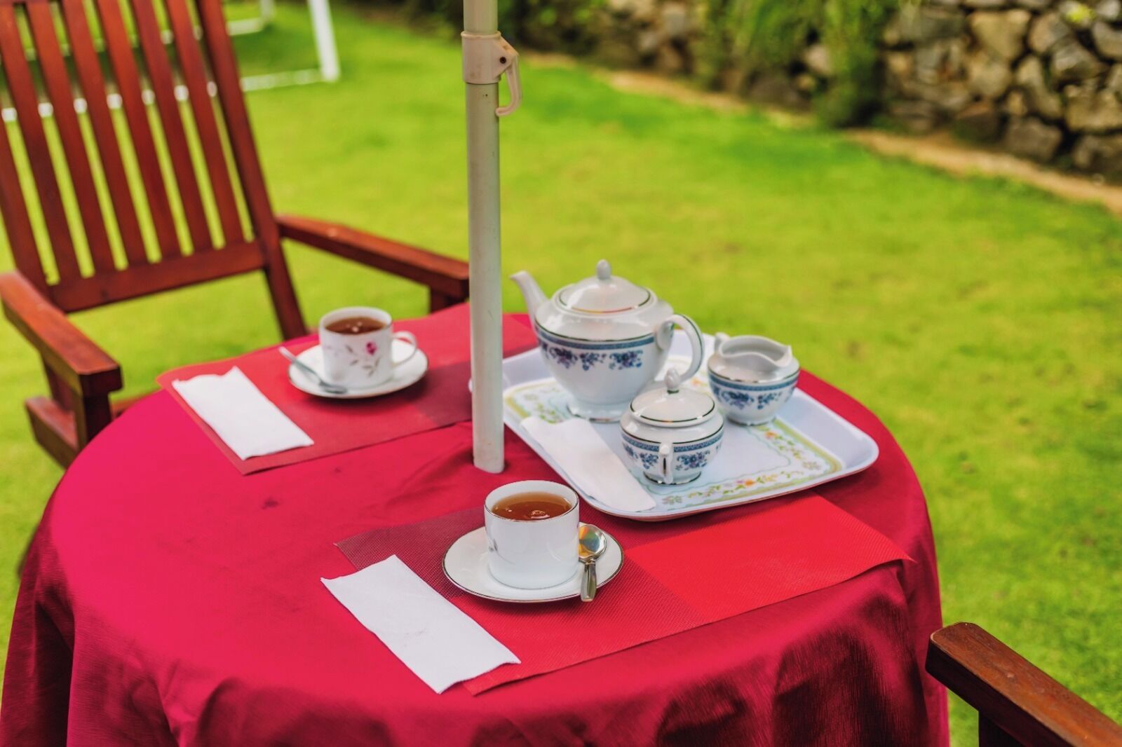 Una mesa cubierta con un mantel rojo, una tetera blanca, dos tazas, una bandeja y una servilleta blanca.