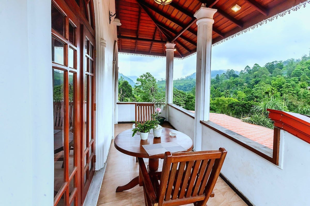 A balcony with a wooden table and chairs, overlooking a lush green landscape.