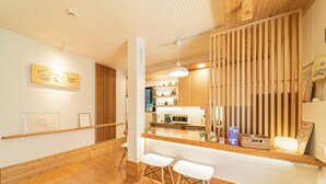 Un intérieur moderne avec un plancher en bois, un comptoir d’accueil, deux tabourets de bar blancs et, au fond, un coin cuisine.