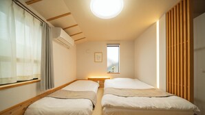 Une chambre avec deux lits, une fenêtre avec des rideaux, un appareil de climatisation et une lambris en bois sur le mur de droite.