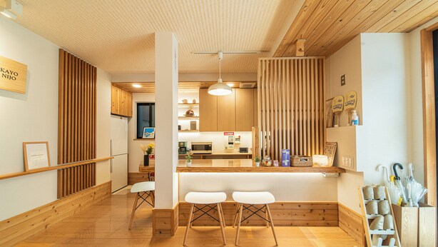 Un intérieur moderne avec un plancher en bois, un comptoir d’accueil, des tabourets de bar blancs et un mur composé de lattes de bois.