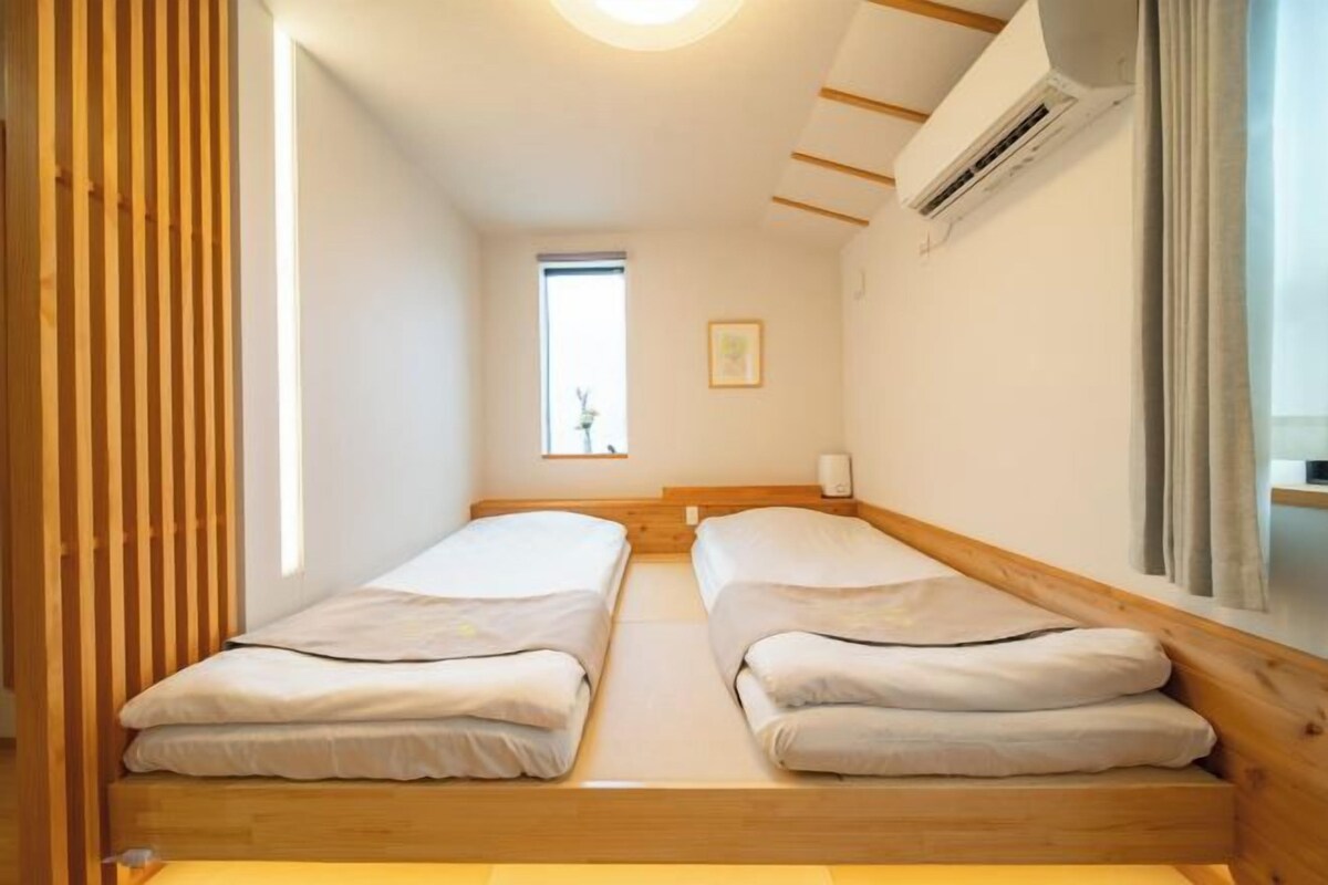 A small, single room with two beds, a window, and a ceiling fan.