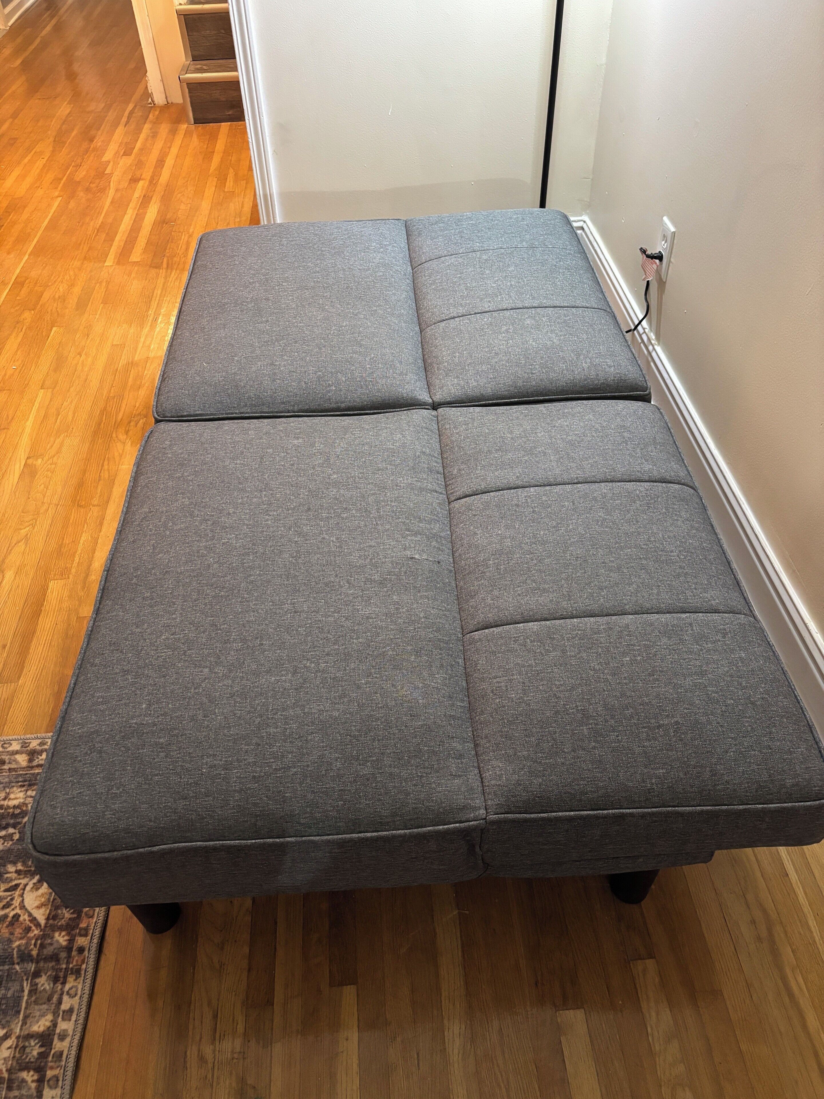 A grey sectional sofa with a wooden floor and a white wall.