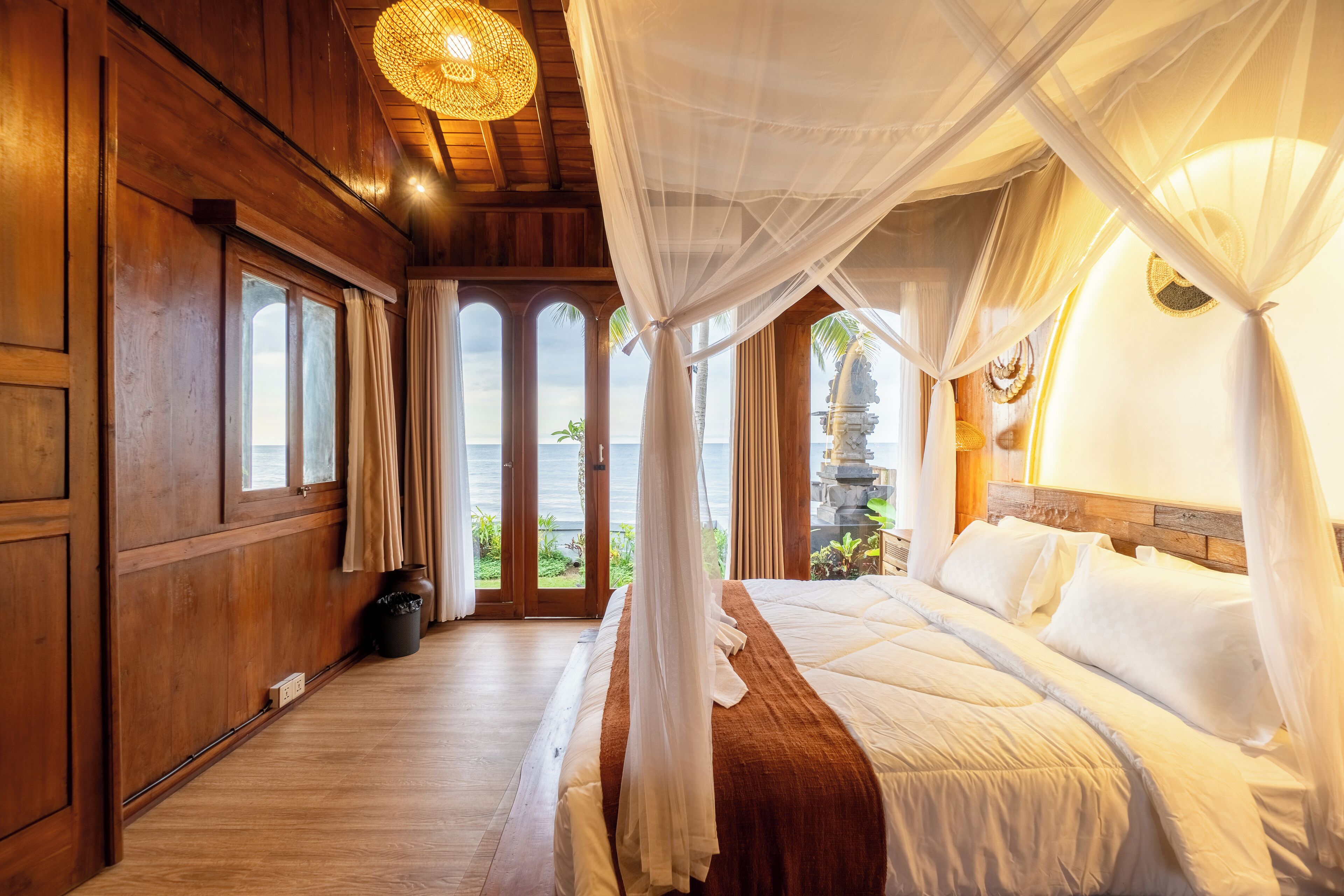 A wooden room with a bed, large windows, and a view of the ocean.