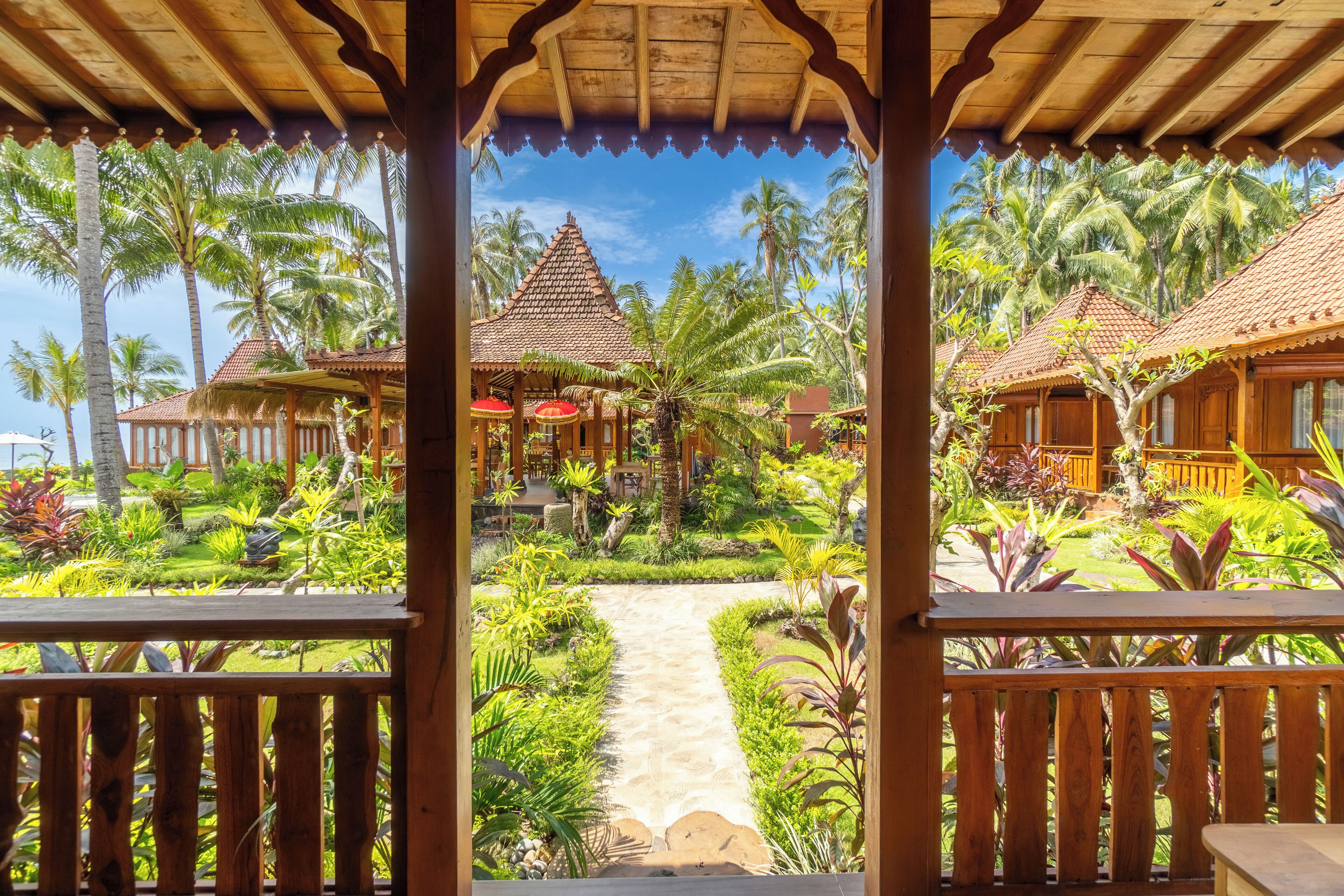 Un complexe hôtelier tropical doté de structures en bois, de palmiers et d’un chemin principal qui le traverse.