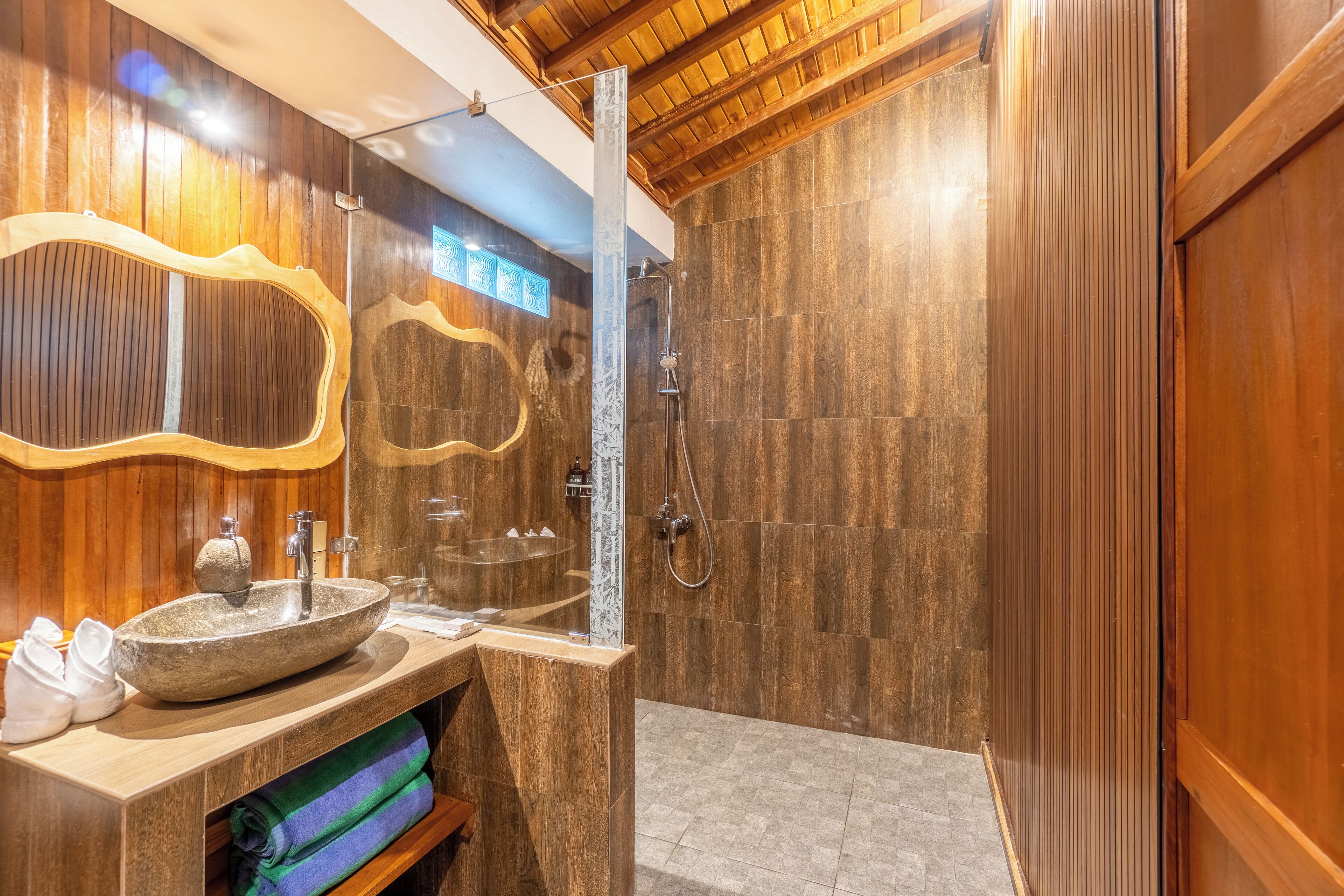 A modern bathroom with a stone sink, wooden vanity, and a shower area.