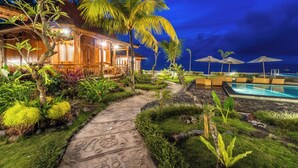 A well-lit resort with a swimming pool, a covered outdoor seating area, and a pathway leading to a building. - Dani Beach Villa Penuktukan (Tejakula)