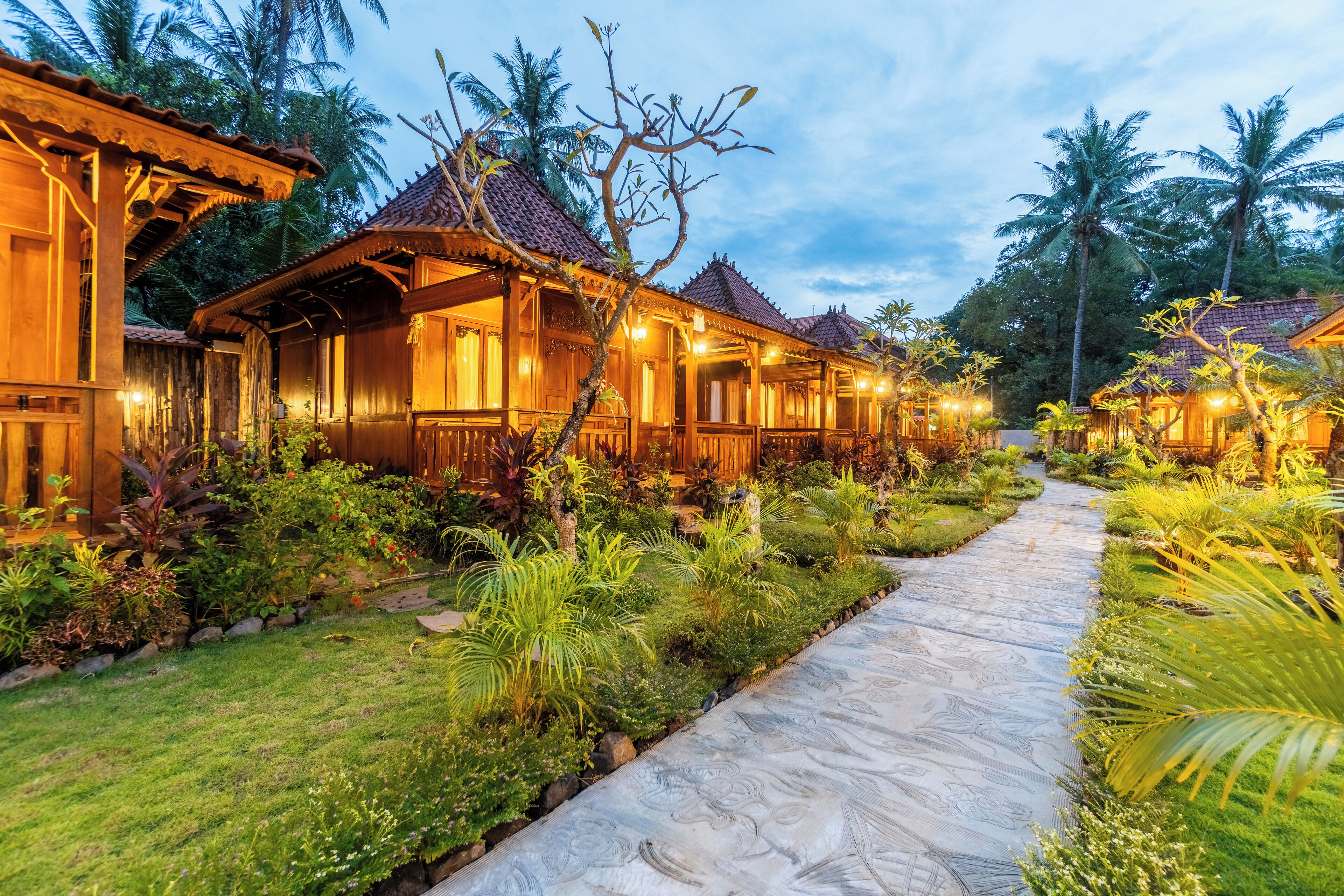 A row of wooden villas with tiled roofs, surrounded by lush greenery and a stone pathway.