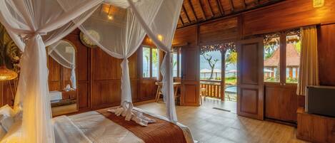 A room with a four-poster bed, wooden flooring, and a view of the outside.
