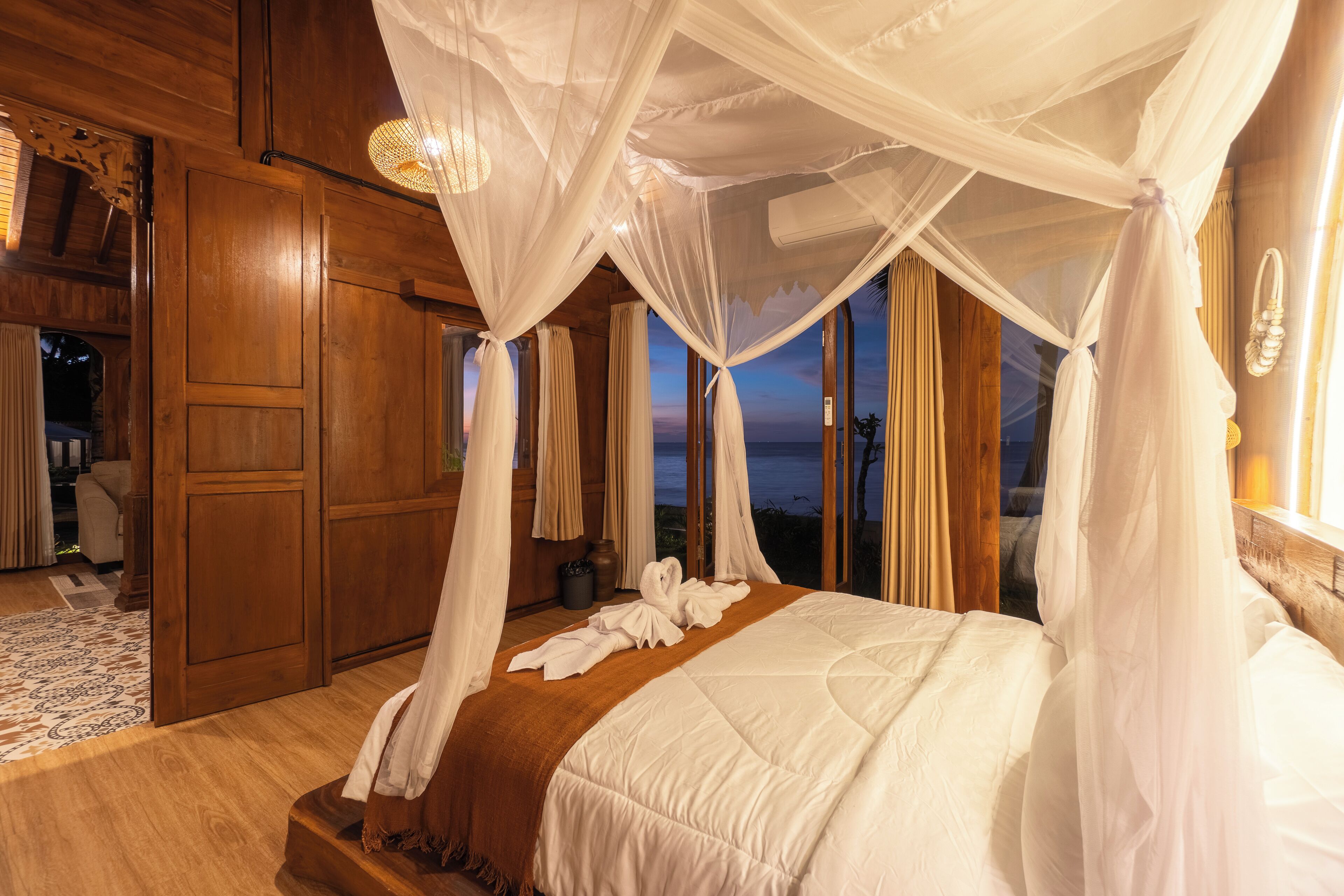 A bedroom with a four-poster bed, wooden walls, and a view of the ocean.