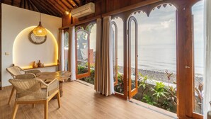 A room with a wooden ceiling, a dining table with wicker chairs, a hanging light fixture, and large windows with curtains. - Dani Beach Villa Penuktukan (Tejakula)