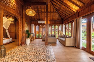 Amplia habitación con techo alto, vigas de madera y grandes ventanales que ofrecen vistas al verdor.