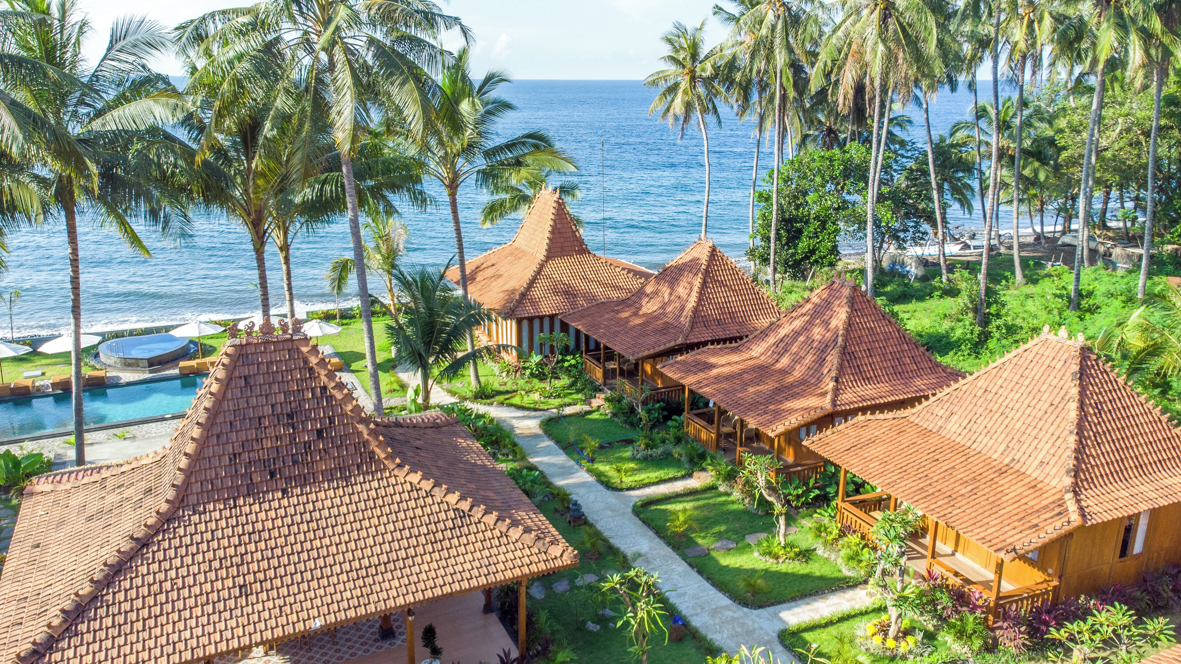 A resort with thatched-roof bungalows, a swimming pool, and a view of the ocean.
