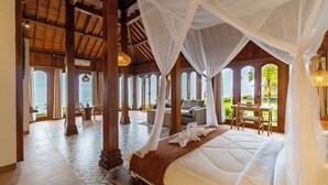 A spacious bedroom with a large bed, a sitting area with a table and chairs, and a view of the outdoors. - Dani Beach Villa Penuktukan (Tejakula)