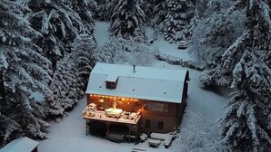 A cabin surrounded by snow-covered trees, with a visible deck and outdoor seating area.