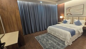 Ein Hotelzimmer mit einem großen Bett, zwei Nachttischen, einer Stehlampe an der Wand und einem großen Fenster mit Vorhängen.